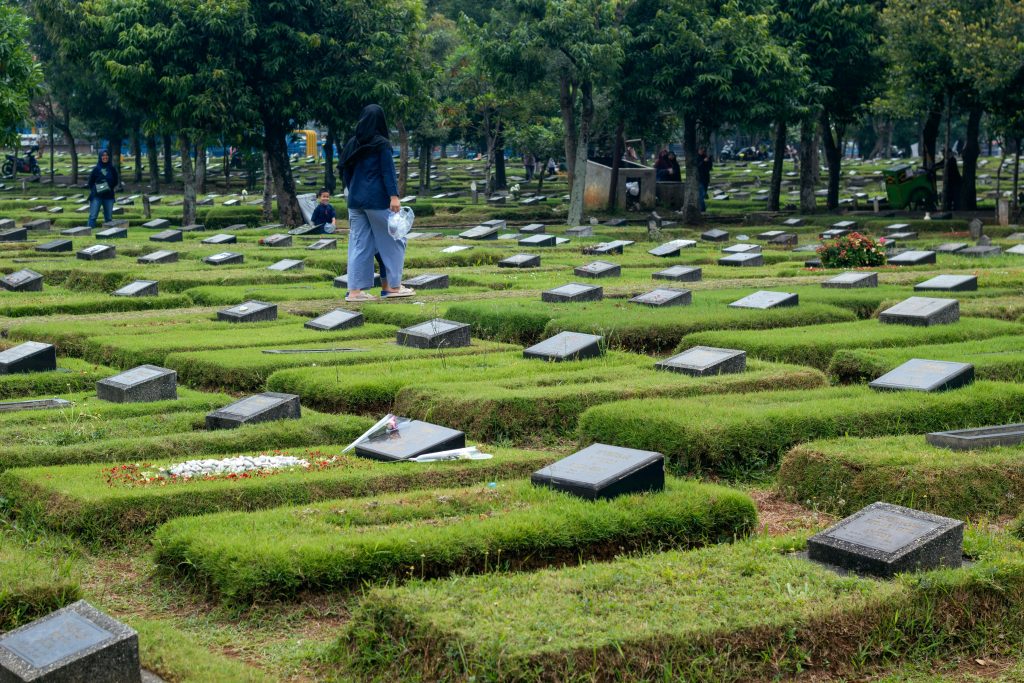A serene view of a Muslim cemetery with tombstones and people mourning in a peaceful setting.